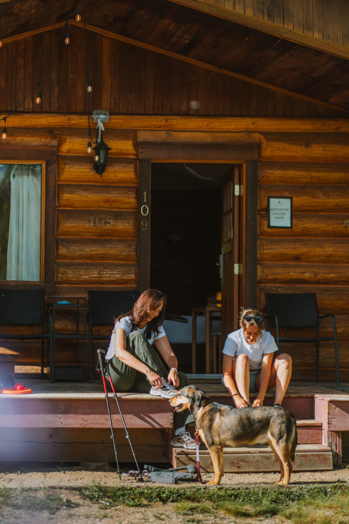 2 hikers and their dog get ready for a hike on the steps of one of the cabins.