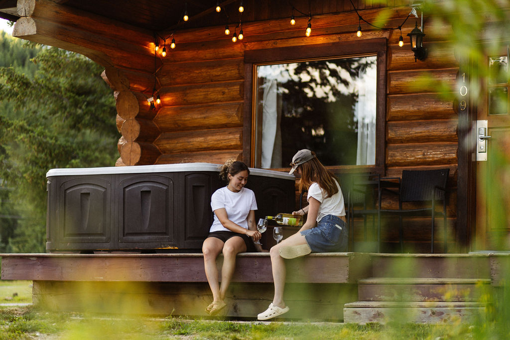 2 women share some wine in front of one of the cabins